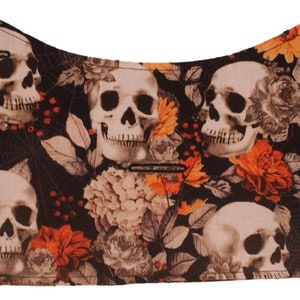 May include: Black fabric with a skull and floral pattern. The fabric features white skulls with black eyes and a black floral pattern with orange, yellow, and white flowers.