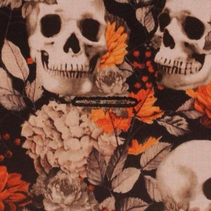 May include: A black fabric with a repeating pattern of white skulls and orange flowers. The skulls have a detailed design and are surrounded by leaves and vines.