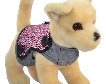Può includere: Un piccolo cane di peluche marrone chiaro che indossa un giubbotto di jeans con un design di paillettes rosa e nero. Il giubbotto ha due bottoni neri.
