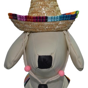May include: A white stuffed dog wearing a straw sombrero with a colorful band. The sombrero has a pink and white string tied around the dog's neck with pink beads.