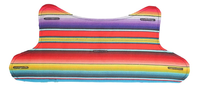 Puede incluir: Una tela de rayas rojas, amarillas, azules y moradas con un borde festoneado. La tela est&aacute; doblada por la mitad y tiene una forma curva.