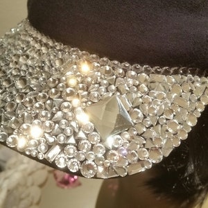 May include: A black cap with a large, sparkly design of rhinestones and crystals. The design is mostly clear with a few silver accents.