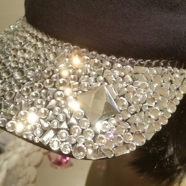 May include: A black cap with a large, sparkly design of rhinestones and crystals. The design is mostly clear with a few silver accents.