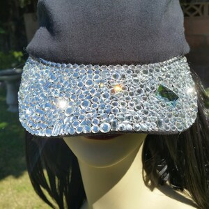 May include: A black baseball cap with a clear rhinestone visor. The rhinestones are arranged in a random pattern.