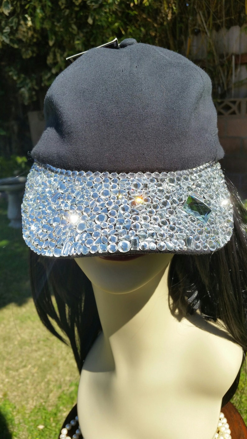 May include: A black baseball cap with a clear rhinestone visor. The rhinestones are arranged in a random pattern.
