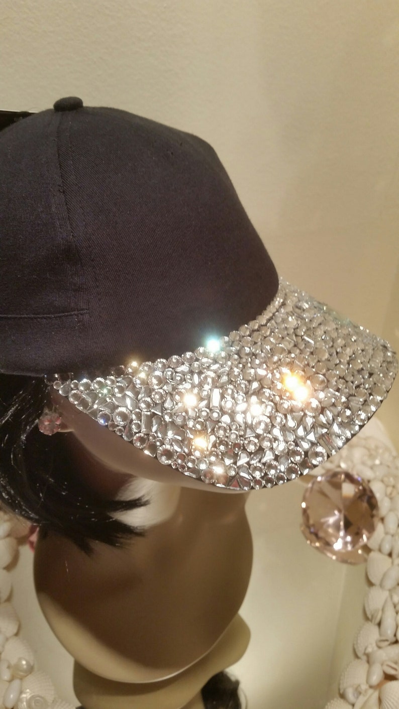 May include: A black baseball cap with a visor covered in clear rhinestones.