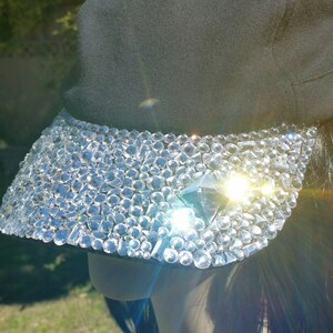 May include: A black baseball cap with a visor covered in clear rhinestones. The rhinestones are arranged in a random pattern and create a sparkling effect.