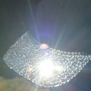 May include: A black baseball cap with a brim covered in clear rhinestones. The rhinestones are arranged in a random pattern and catch the light.