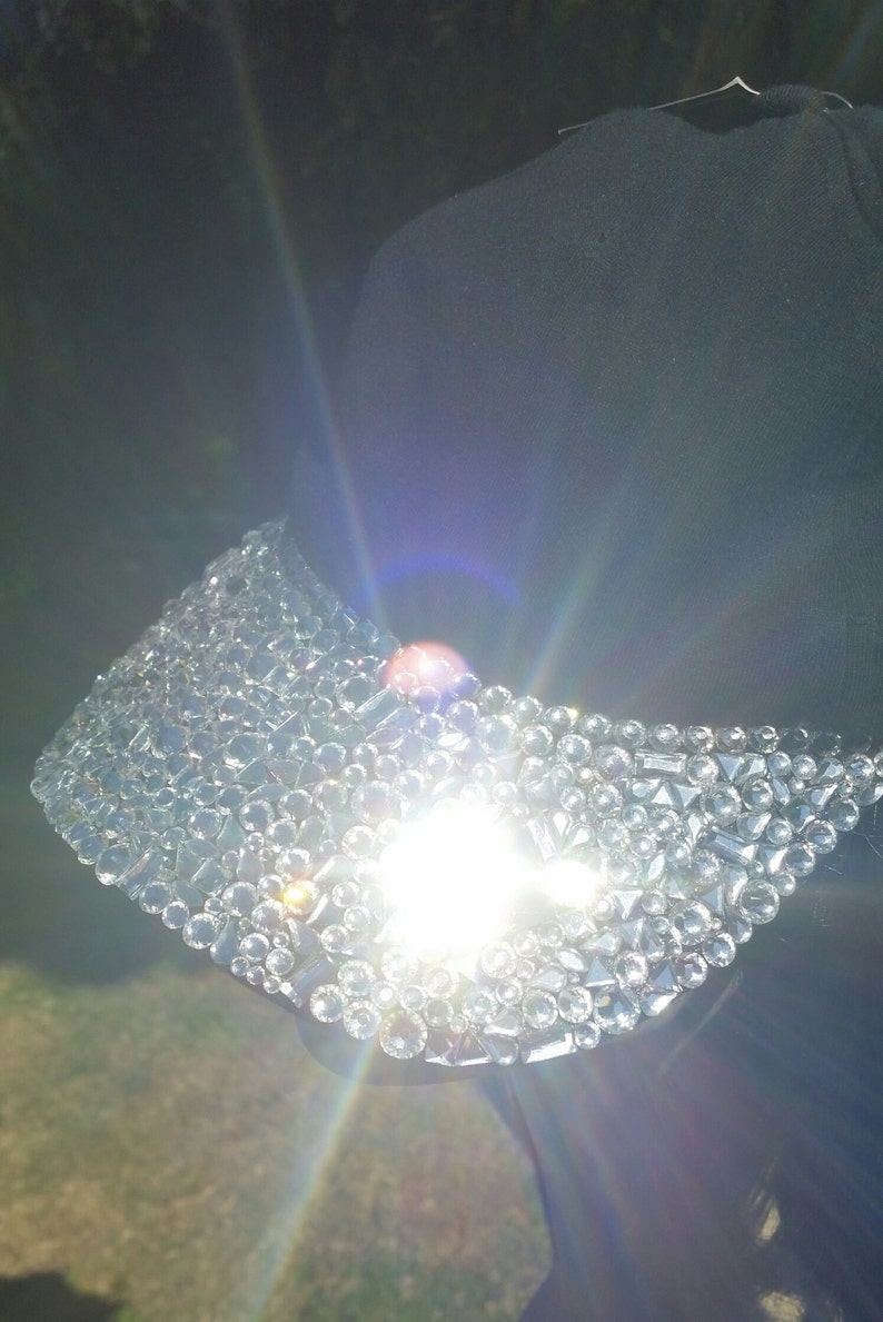 May include: A black baseball cap with a brim covered in clear rhinestones. The rhinestones are arranged in a random pattern and catch the light.