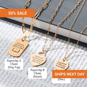 May include: Three gold-toned necklaces with varying pendants and chain styles. One features a rectangular dog tag with an open book icon and text, one a heart-shaped pendant with engraved text, and one a circular disc with engraved text.