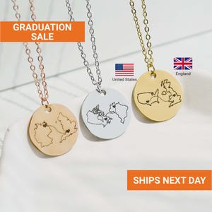 May include: Three necklaces with round pendants, each featuring a map design. One is gold-toned with a map of England, another is silver-toned with a map of Canada and the United States, and the third is gold-toned with a map of Germany. The text "GRADUATION SALE" is visible.