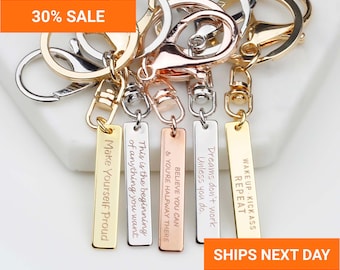 May include: Five metal keychains with lobster claw clasps and rectangular tags in gold, silver, and rose gold tones. Each tag is engraved with motivational text including Make Yourself Proud, This is the beginning of anything you want, Believe you can, Dreams don't work unless you do, and Wake Kickass Repeat.