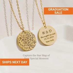 May include: Two gold-colored pendant necklaces. One pendant features a star map design, and the other is engraved with initials, a date, and a location. The text "GRADUATION SALE" and "SHIPS NEXT DAY" are also visible.