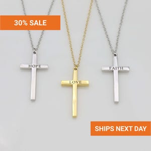 Three cross necklaces with different messages engraved on them, displayed against a white background.