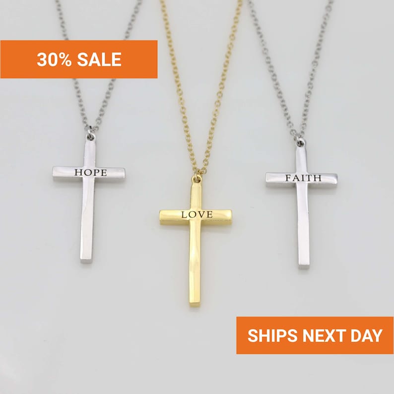 Three cross necklaces with different messages engraved on them, displayed against a white background.