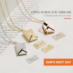 May include: Two metal envelope pendants on chains, one gold and one silver. The gold pendant is open, revealing a small metal insert. Three additional rectangular metal tags are displayed, engraved with "L A 02.14.2000", "Love you more", and "You're my sunshine".