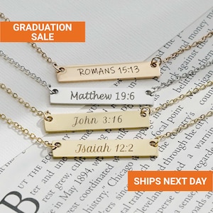 May include: Four gold and silver bar necklaces with engraved Bible verses: Romans 15:13, Matthew 19:6, John 3:16, and Isaiah 12:2. The necklaces are displayed on a printed background with the text "GRADUATION SALE".
