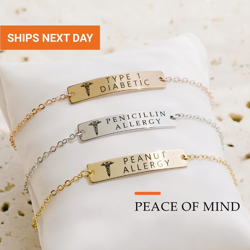 May include: Three medical alert bracelets with thin metal chains and rectangular plates. The top plate is gold-toned with 'TYPE 1 DIABETIC' text, the middle is silver-toned with 'PENICILLIN ALLERGY', and the bottom is gold-toned with 'PEANUT ALLERGY'.
