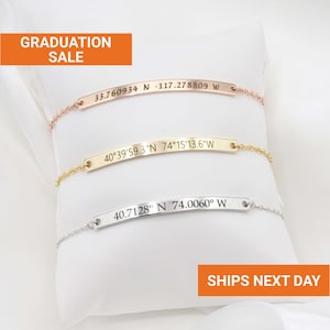 May include: Three delicate bracelets with engraved coordinates in rose gold, gold, and silver. The bracelets are displayed on a white pillow. The image includes the text "GRADUATION SALE" and "SHIPS NEXT DAY".