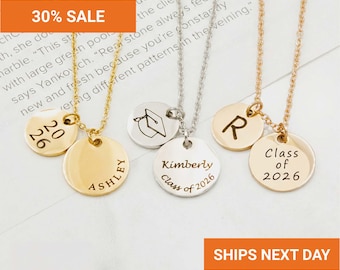 May include: Three metal necklaces with circular pendants. The first is gold with '2026' and 'ASHLEY' engraved. The second is silver with a graduation cap icon, 'Kimberly', and 'Class of 2026'. The third is gold with an 'R' and 'Class of 2026' engraved.
