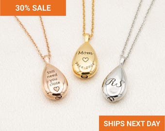 May include: Three teardrop-shaped cremation urn pendants on delicate chains in rose gold, yellow gold, and silver tones. The rose gold pendant is engraved with Still need you close and a heart. The yellow gold pendant reads Mom, a heart, and 1966-2006. The silver pendant features the initials RS.