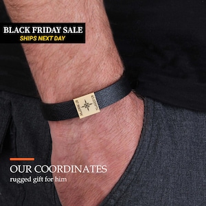 A close-up of a person's arm wearing a black leather bracelet with a gold-colored charm.