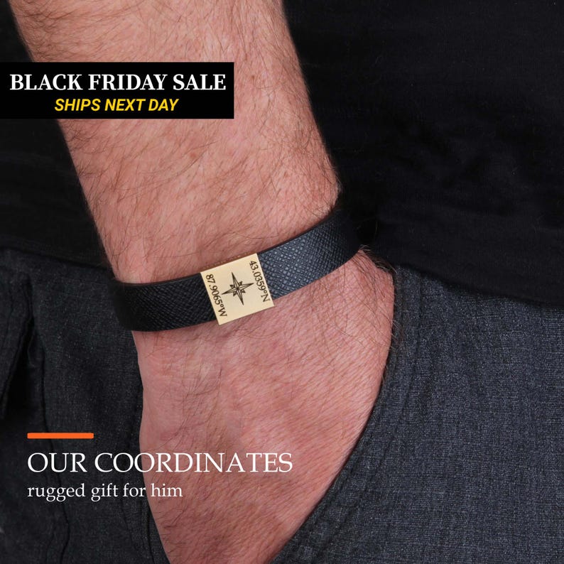 A close-up of a person's arm wearing a black leather bracelet with a gold-colored charm.
