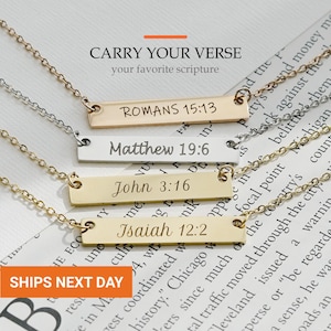 May include: Four metal bar necklaces with delicate chains, each engraved with a different scripture reference: ROMANS 15:13, Matthew 19:6, John 3:16, and Isaiah 12:2. The necklaces feature gold and silver tones and are displayed on a printed page.
