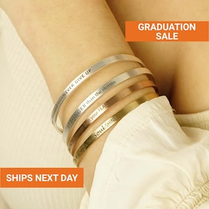 May include: A collection of five metal bracelets in silver, rose gold, and gold tones. Each bracelet is engraved with an inspirational message, including "NEVER GIVE UP" and "STRONGER than the storms." The image also includes the text "GRADUATION SALE."