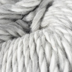 May include: Close-up of a skein of thick, chunky yarn in shades of gray and white. The yarn has a soft, textured appearance, with visible strands and a braided structure. Ideal for knitting or crocheting projects.