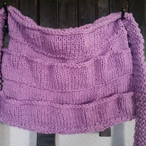 May include: A lavender knitted scarf with long sleeves. The scarf is made with a simple stitch pattern and has a relaxed, drapey look.