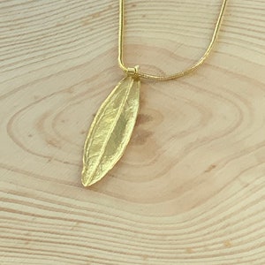 K&ouml;nnte beinhalten: Eine goldene Kettenkette mit einem blattartigen Anh&auml;nger. Der Anh&auml;nger ist aus Metall und hat ein detailliertes Design.