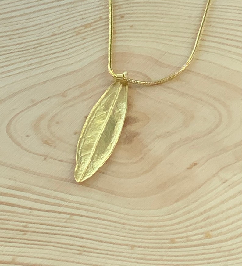 K&ouml;nnte beinhalten: Eine goldene Kettenkette mit einem blattartigen Anh&auml;nger. Der Anh&auml;nger ist aus Metall und hat ein detailliertes Design.