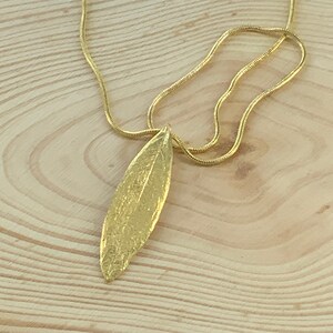 K&ouml;nnte beinhalten: Eine goldene Kettenkette mit einem strukturierten goldenen Blattanh&auml;nger.