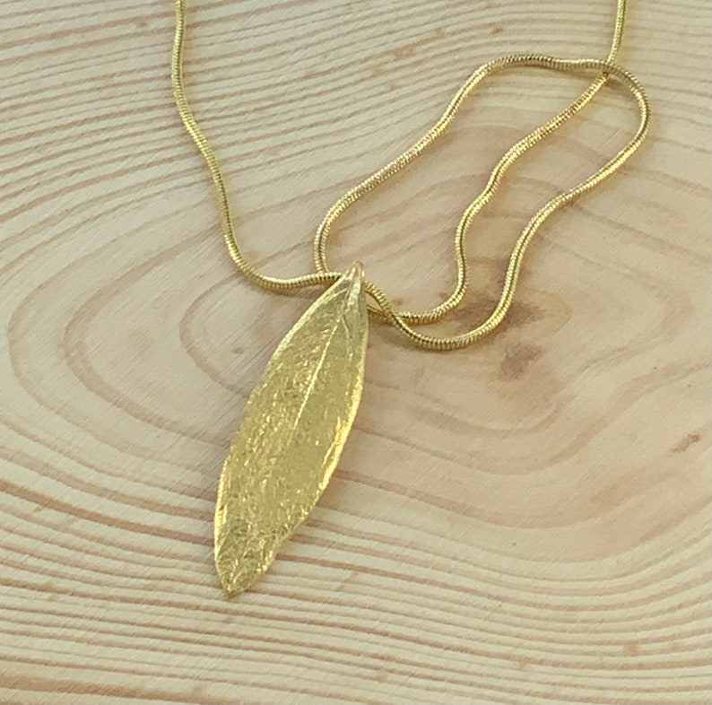 K&ouml;nnte beinhalten: Eine goldene Kettenkette mit einem strukturierten goldenen Blattanh&auml;nger.
