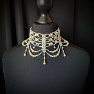 May include: An elegant ivory pearl choker necklace with multiple layers and dangling pearl accents. The necklace is displayed on a black mannequin, showcasing its intricate design and delicate details. The necklace is a statement piece.