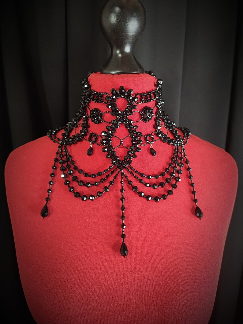 May include: A black beaded choker necklace with a delicate, intricate design. The necklace features multiple layers of beads and dangling drops, creating a dramatic and elegant look.