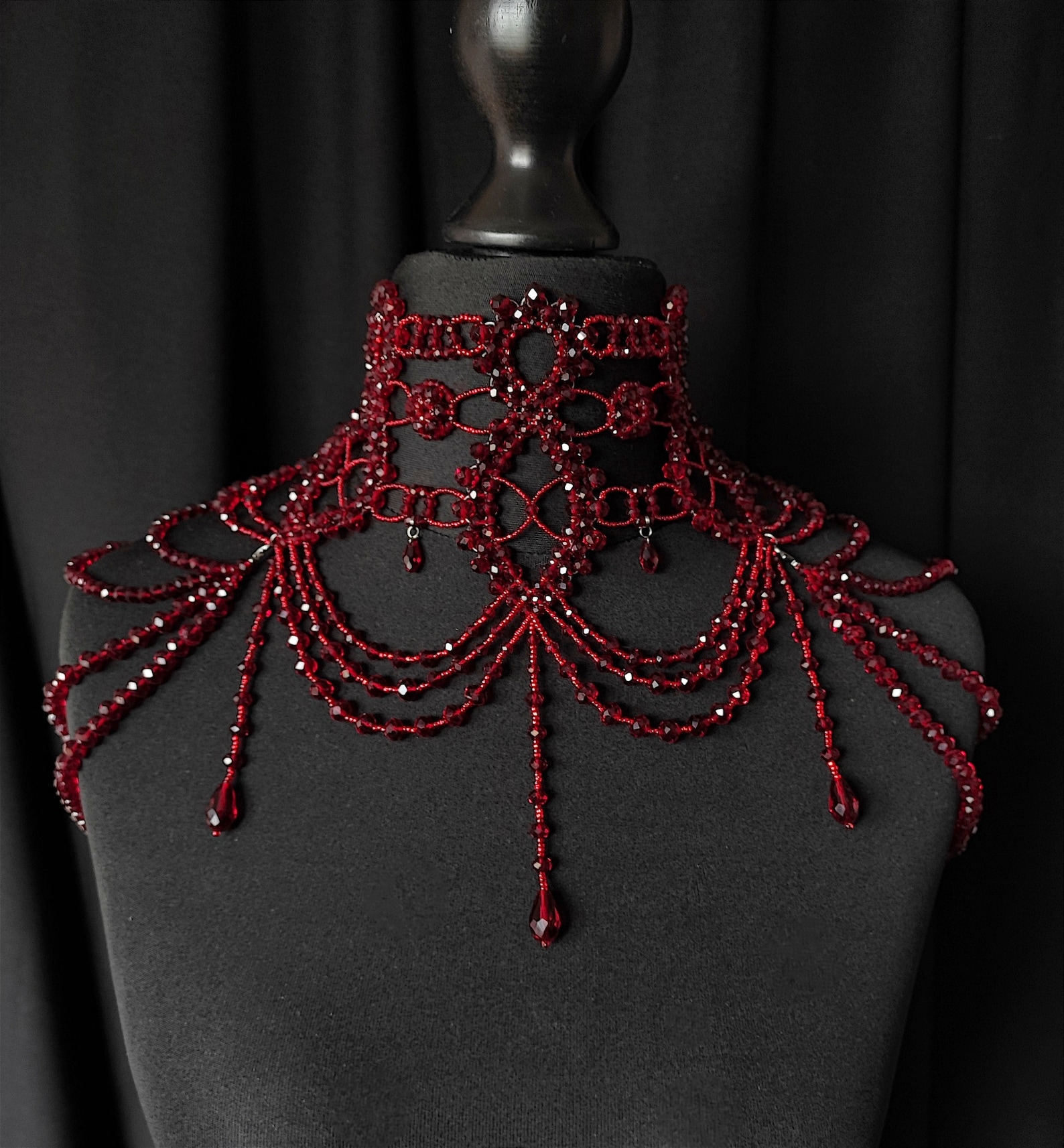 Red crystal shoulder necklace with elaborate festoon draping on black mannequin bust.