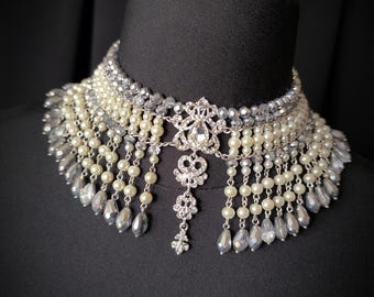 May include: A silver and white beaded choker necklace with a large silver pendant and a cascading fringe of beads.