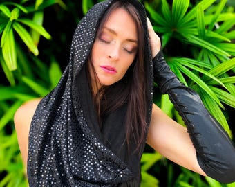 May include: A black sequined hooded scarf and matching arm sleeves. The scarf is draped over the head and shoulders, with the sequins catching the light. The sleeves are long and form-fitting, creating a dramatic look.