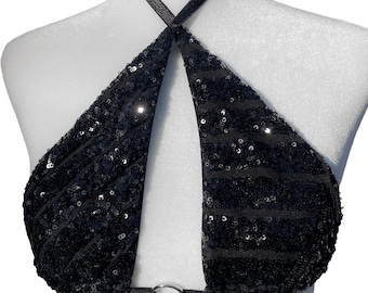 May include: A black halter top covered in shimmering sequins, featuring a triangular design with a central silver-toned metal ring connecting the two front panels at the base. The garment has thin black straps that tie around the neck.
