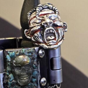 May include: A silver bracelet with a skull charm and a detailed silver charm of a snarling face with red accents.
