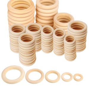 Puede incluir: Una colección de anillos de madera sin terminar en varios tamaños. Los anillos están apilados en columnas y filas, con tamaños que van desde 15 mm hasta 55 mm. El color natural de la madera es visible, y los anillos son lisos.