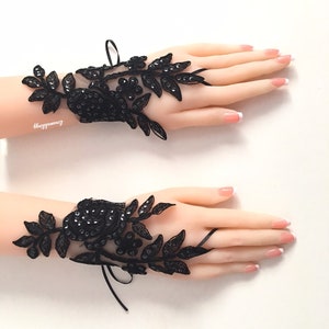Pode incluir: Um par de luvas sem dedos de renda preta com um design floral e contas pretas. As luvas t&ecirc;m um la&ccedil;o de fita no pulso.