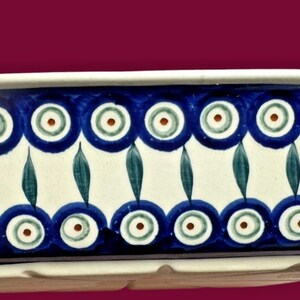 May include: A rectangular ceramic baking dish featuring a cream-colored base with a hand-painted pattern of dark blue concentric circles and green leaf-like motifs arranged in horizontal bands around the exterior side walls.