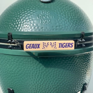 May include: Green Big Green Egg grill with a wooden handle that says "Geaux Tigers" in purple lettering.