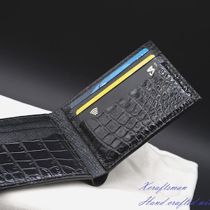 May include: A black bifold wallet featuring a textured crocodile skin pattern on the exterior and interior. The wallet is open, revealing multiple card slots with a black payment card inserted. The text Xeraftsman Hand crafted is visible.