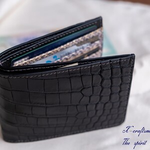 Puede incluir: Una cartera de cuero negro con un patr&oacute;n de cocodrilo. La cartera est&aacute; abierta y muestra varias tarjetas en el interior.