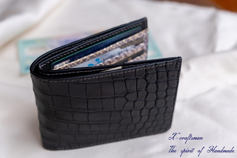 Puede incluir: Una cartera de cuero negro con un patr&oacute;n de cocodrilo. La cartera est&aacute; abierta y muestra varias tarjetas en el interior.
