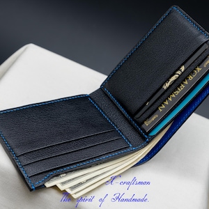May include: A black leather wallet with blue stitching and a blue interior. The wallet is open and has several cards and cash inside.